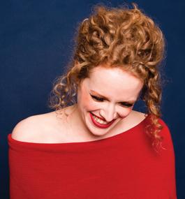 A photo of Kristen Lee Sergeant wearing an off-the-shoulder red top, smiling and looking down.